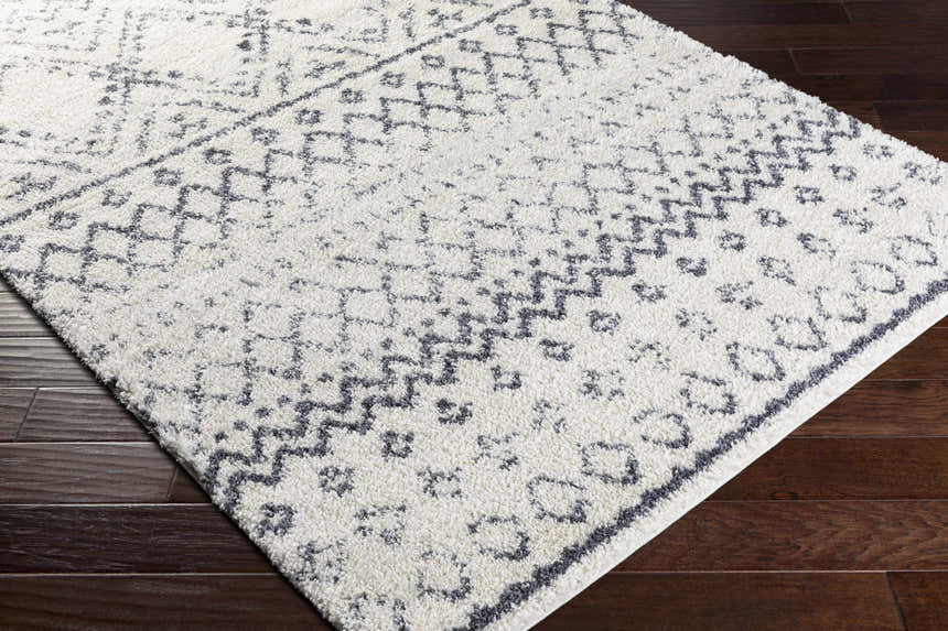 Close up of the Benezett Area Rug. White shag rug with gray bohemian pattern on dark wood floor. Corner