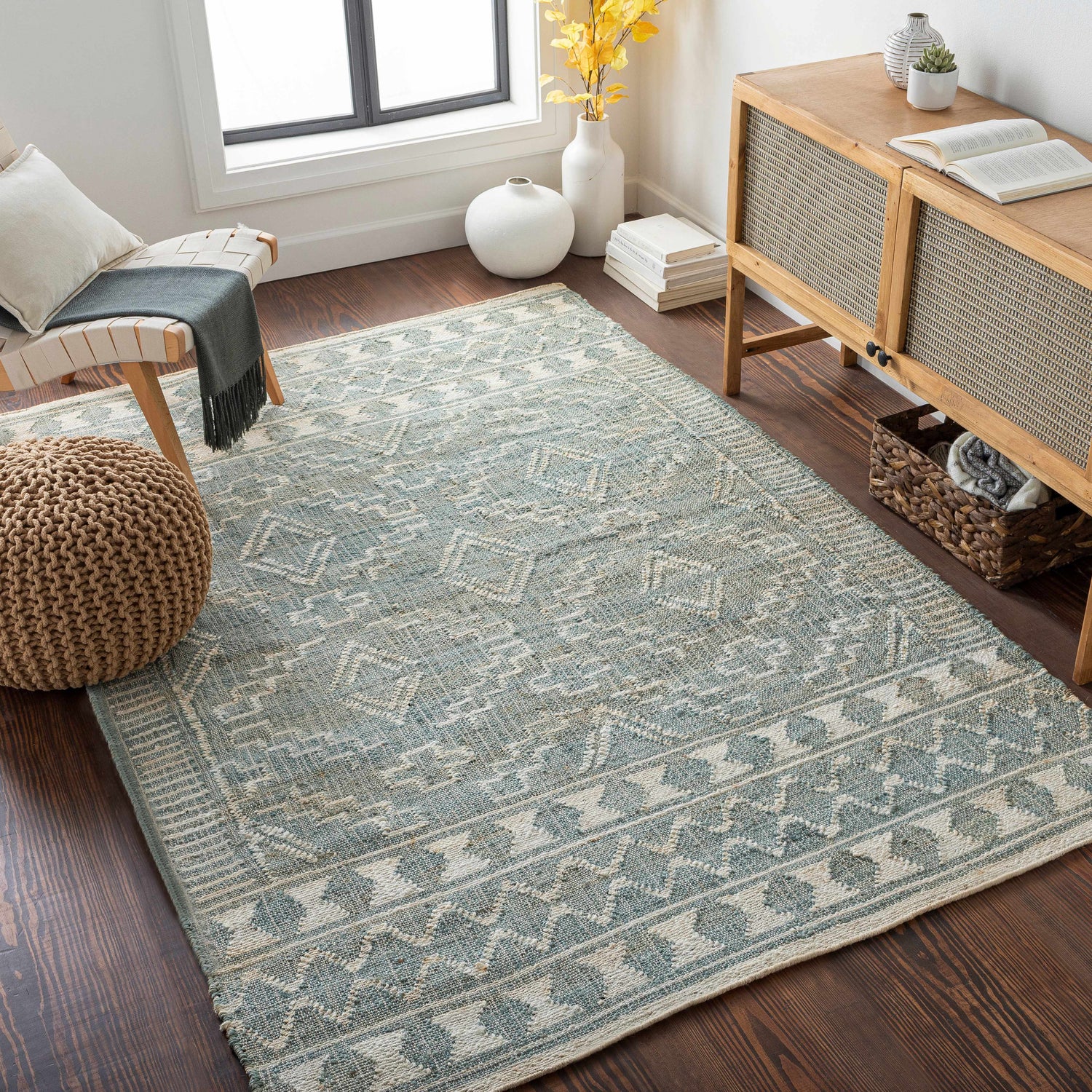 Living room scene with a Berowra Jute Rug in dusty sage and ivory, styled with a chair, ottoman, and wooden cabinet. Roomscene-Rectangle