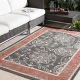 Outdoor patio scene with a black wicker sofa and the Berryman Area Rug in black and brick red. Roomscene-Rectangle