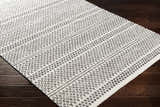 Close-up of Bewbush Washable Area Rug. Cream cotton rug with black bohemian pattern on dark wood floor. Corner