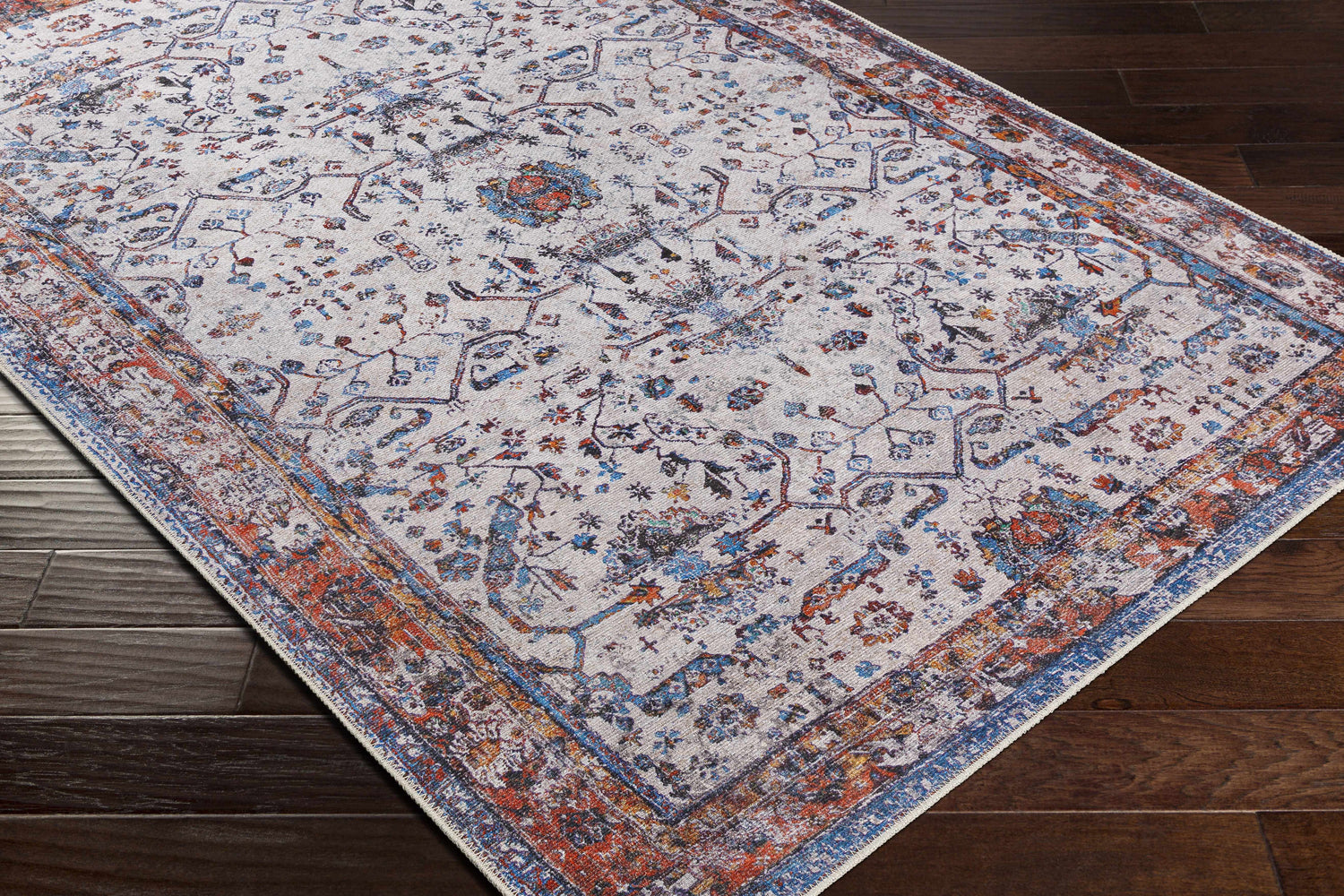 Close-up of Beykonak Washable Area Rug. Vintage style rug with black, blue, orange, and light gray floral pattern. Corner