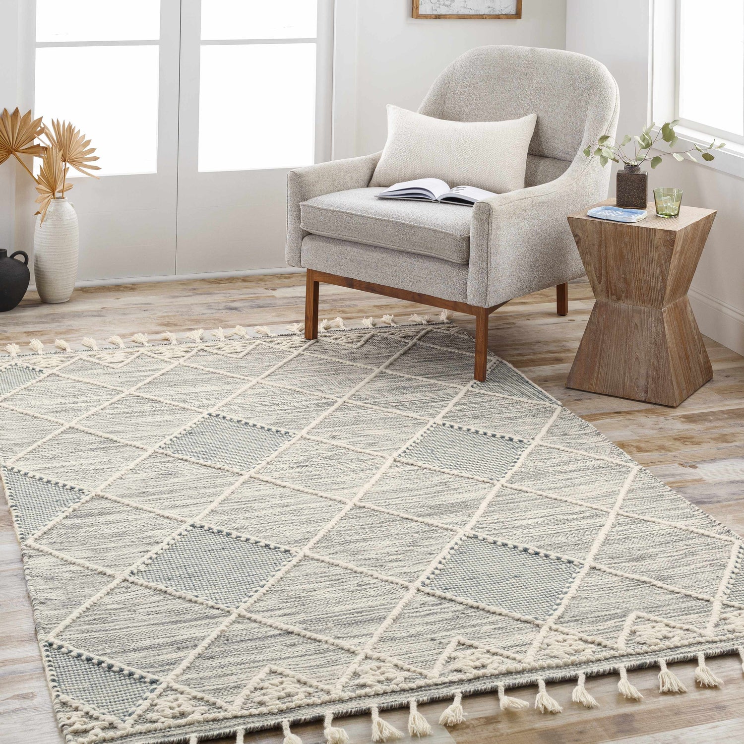 Living room scene with Bicos Tasseled Jute Rug in charcoal and cream, light gray chair, and wood side table. Roomscene-Rectangle
