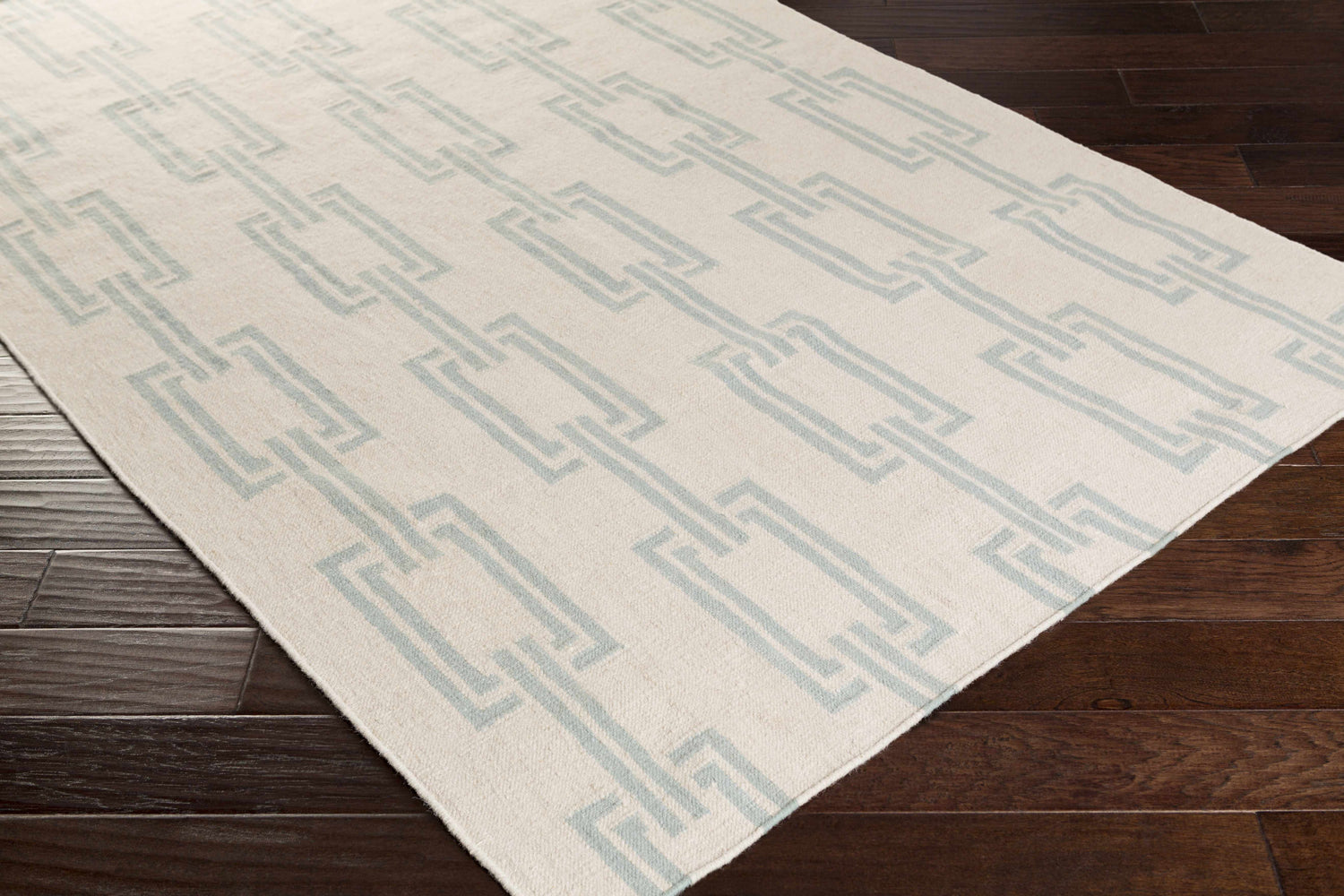 Close-up of Billerica Area Carpet in beige and dusty sage. Hand-woven wool rug with a contemporary geometric chain pattern. Corner
