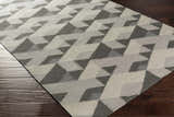 Close-up of a Birchleaf Area Carpet. Hand-woven wool rug in charcoal, gray, ivory geometric pattern on a dark wood floor. Corner