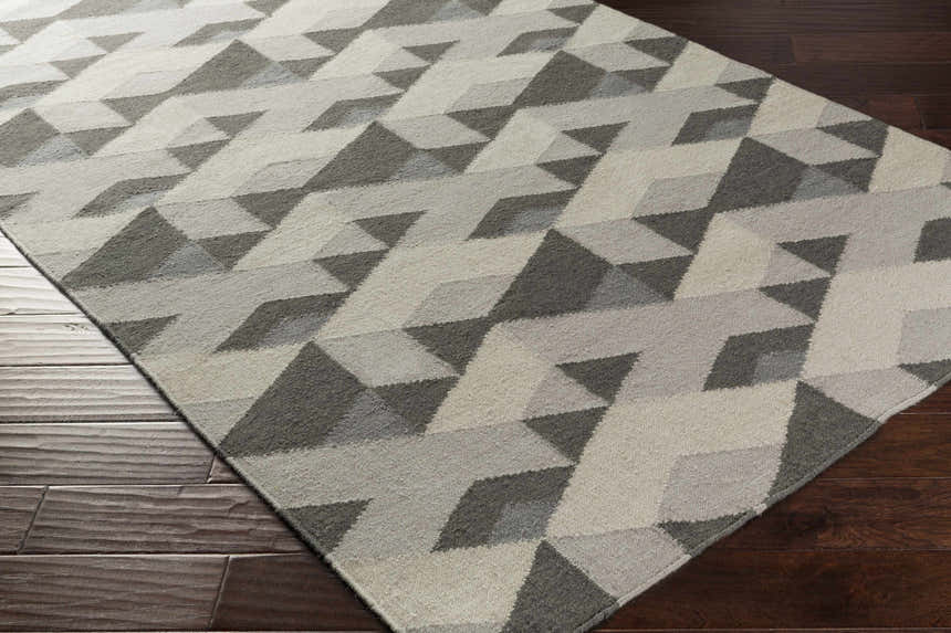 Close-up of a Birchleaf Area Carpet. Hand-woven wool rug in charcoal, gray, ivory geometric pattern on a dark wood floor. Corner