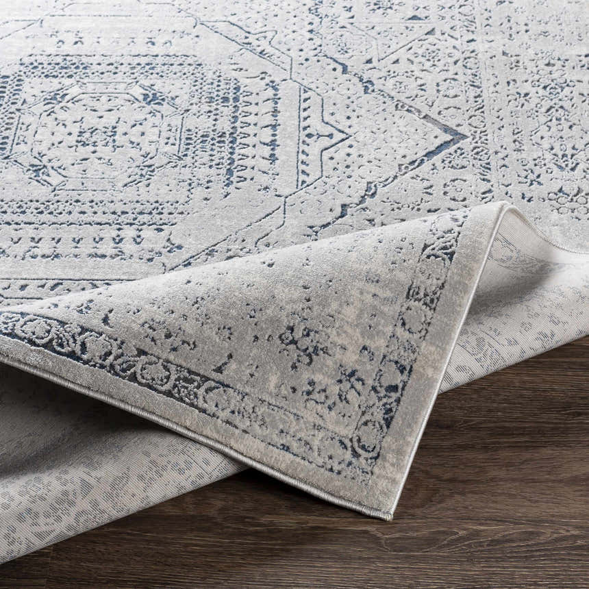 Close-up of Blantyre Faux Silk Rug in gray and navy on dark wood floor, showing traditional Oriental pattern and soft texture. Fold