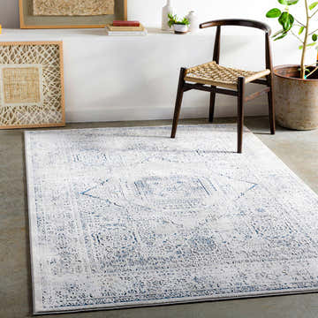 Living room scene with a gray and navy Blantyre Faux Silk Rug, wooden chair, and neutral decor. Roomscene-Rectangle