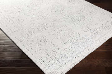 Close-up of the Blackfoot Area Rug showing its white and black farmhouse design and hand-knotted texture on dark wood floors. Corner