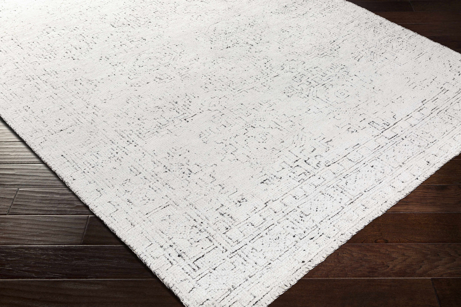 Close-up of the Blackfoot Area Rug showing its white and black farmhouse design and hand-knotted texture on dark wood floors. Corner