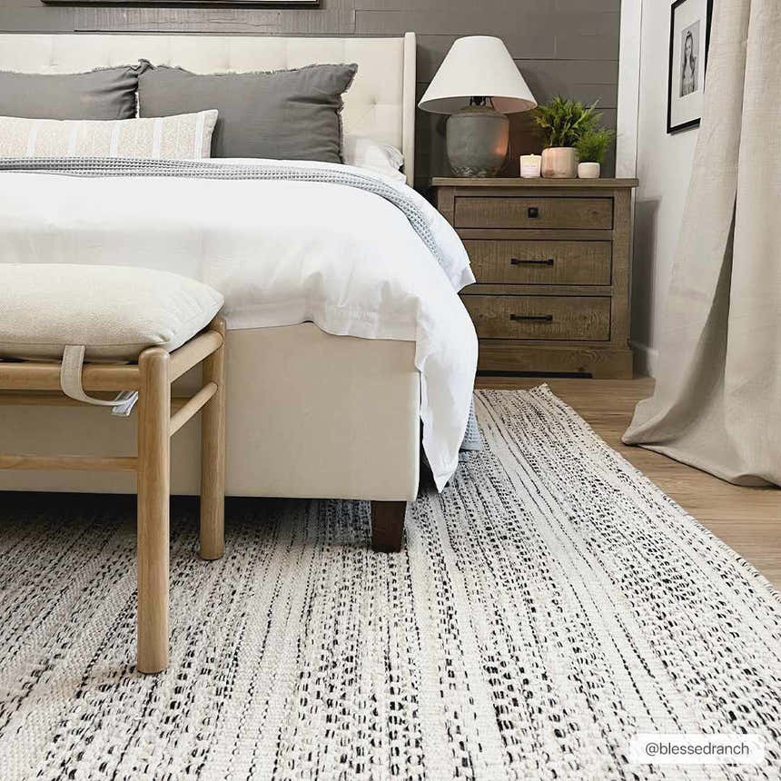Bedroom scene with a black and cream Williford Wool Area Rug, white bed, wooden bench and nightstand. Roomscene-Rectangle