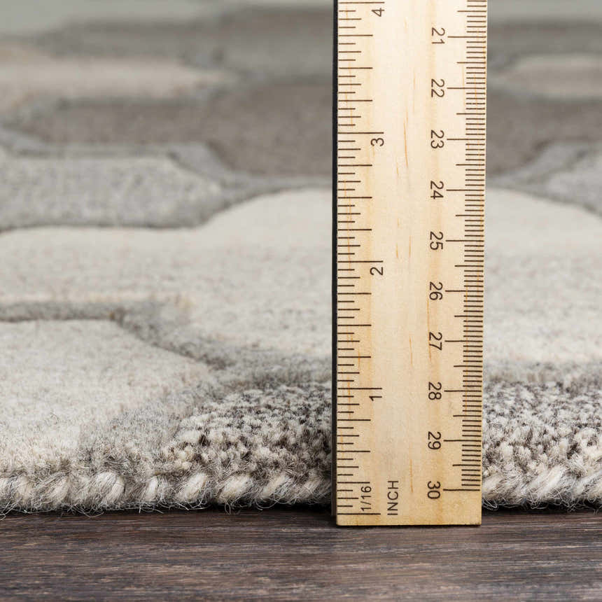 Close-up of Bluffdale rug texture. Hand-tufted 100% wool rug in beige and gray with a geometric pattern. Ruler shows rug thickness. Pile