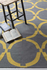Close-up of gray and mustard Bloomer Area Rug with geometric design, styled with books and a stool. Styleshot