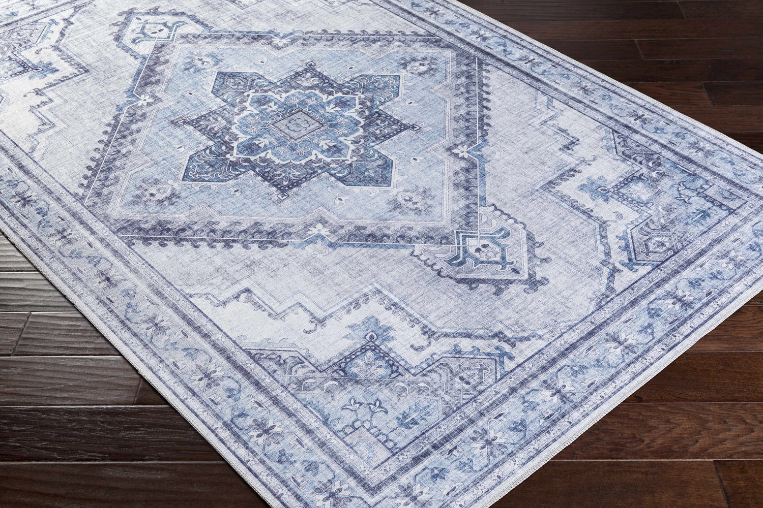 Close-up of the Boon Area Rug, a traditional design in ivory, medium gray, navy, and pale blue on dark wood flooring. Corner