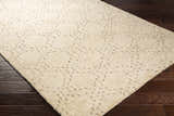 Close-up of the hand-knotted Banksia Area Rug. Cream wool rug with subtle brown geometric pattern on dark wood floor. Corner