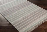 Close-up of the hand woven Bocana Area Rug. Gray, light beige, peach, sage, and seafoam stripes with fringe on dark wood floor. Corner