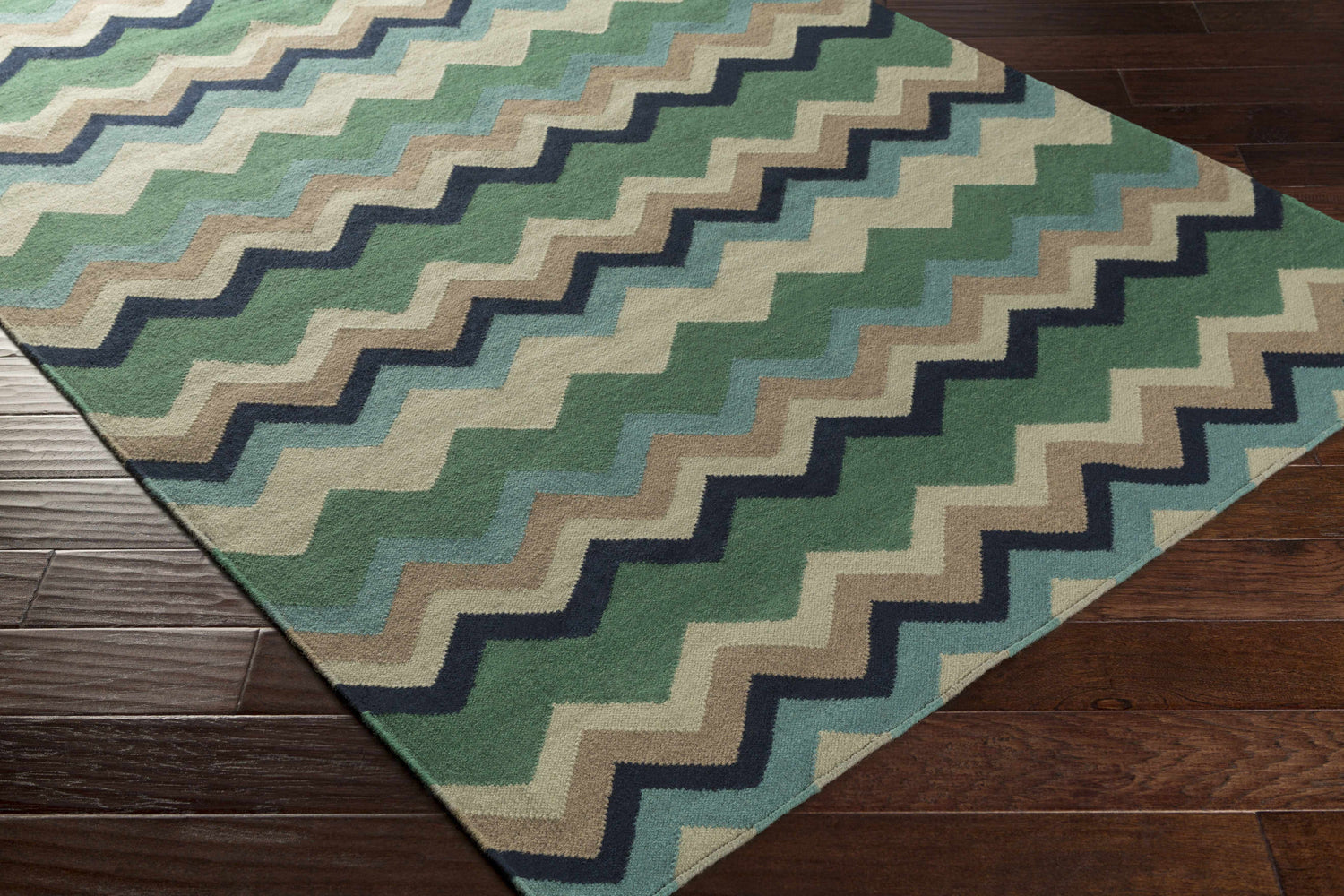 Close-up of the hand woven Bogota Area Rug. Features a contemporary beige, blue, brown, and green zigzag pattern. Corner