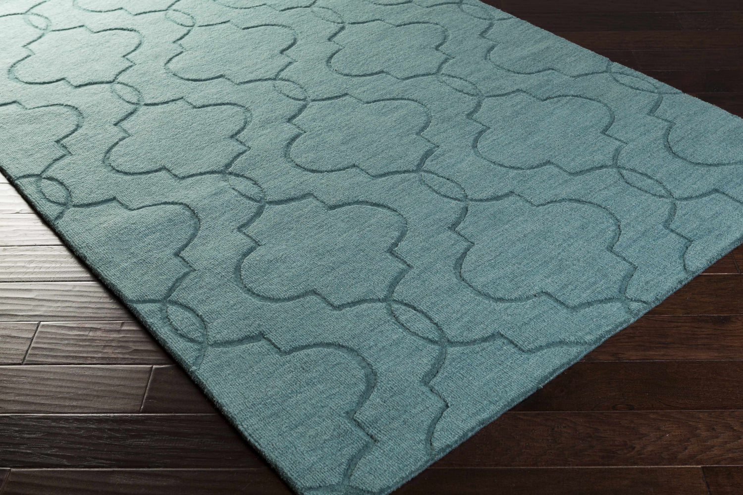 Close-up of the denim Bountiful Area Rug. Hand-loomed wool rug with a contemporary quatrefoil pattern on dark wood floors. Corner