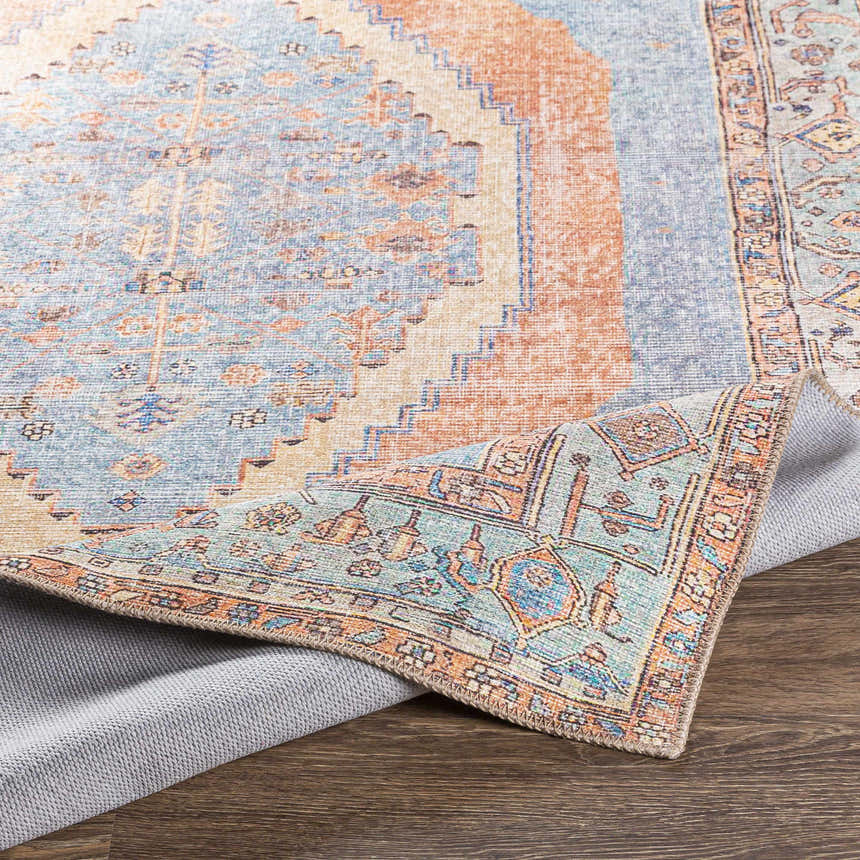 Close-up of the Bovey Washable Area Rug showing its aqua, coral, and blue traditional design and textured gray backing. Fold
