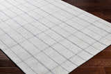 Close-up of the hand woven Brava Area Rug. Light gray with a dark gray plaid pattern on dark brown wood floors. Corner
