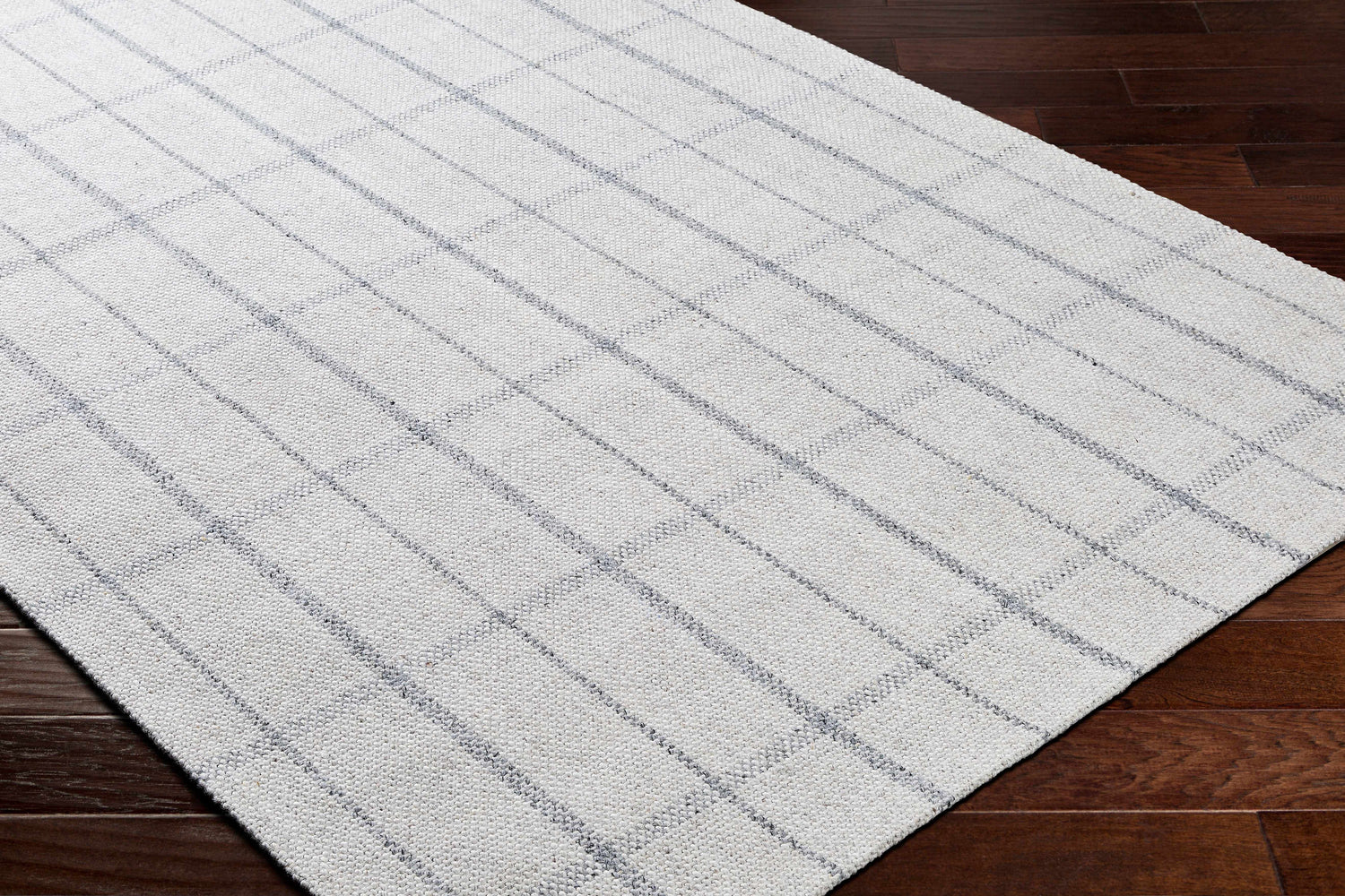 Close-up of the hand woven Brava Area Rug. Light gray with a dark gray plaid pattern on dark brown wood floors. Corner