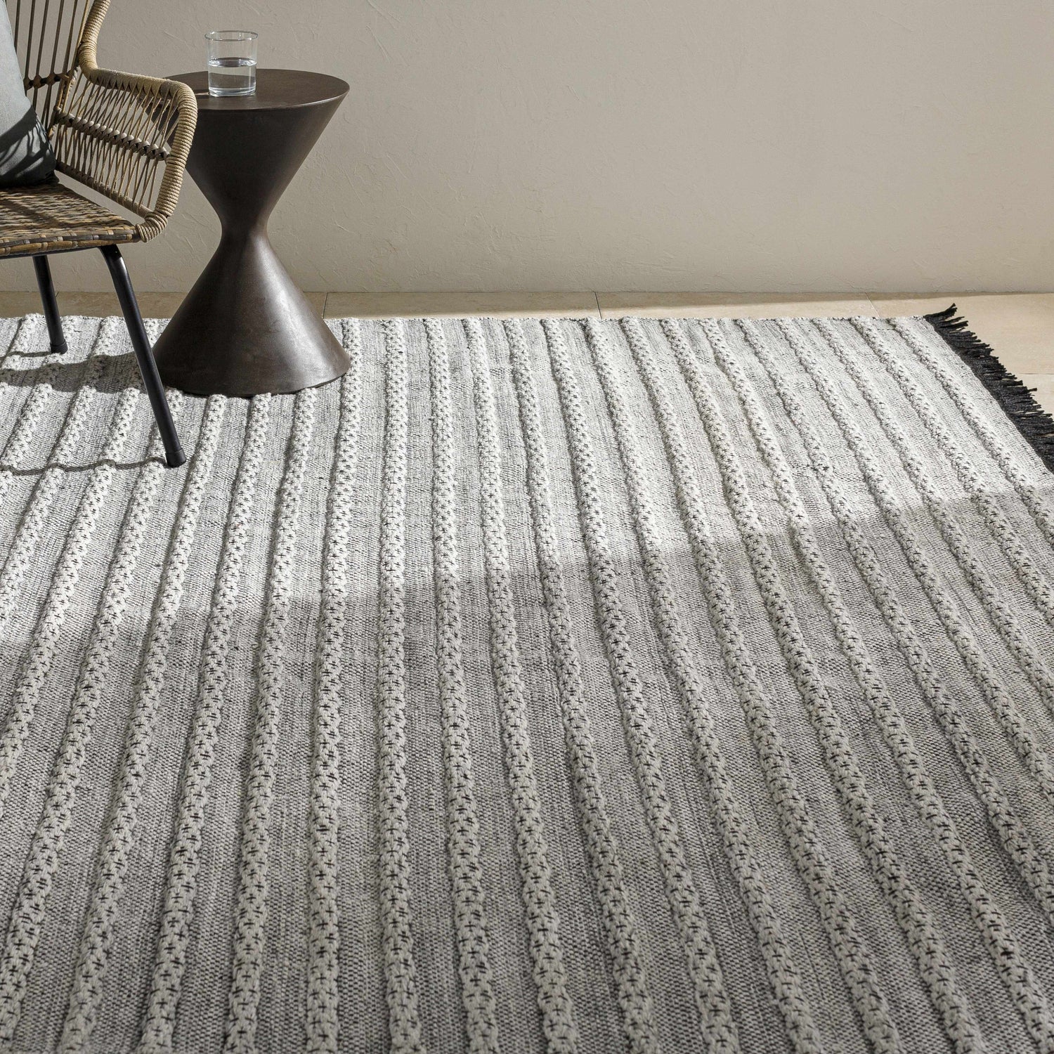 Neutral room scene with a gray and off-white striped Brockman Area Rug, woven chair, and small accent table. Styleshot