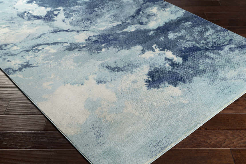 Close-up of Bright Sky Indoor/Outdoor Rug. Coastal style rug with ivory, light slate, navy, and pale blue cloud-like design. Corner