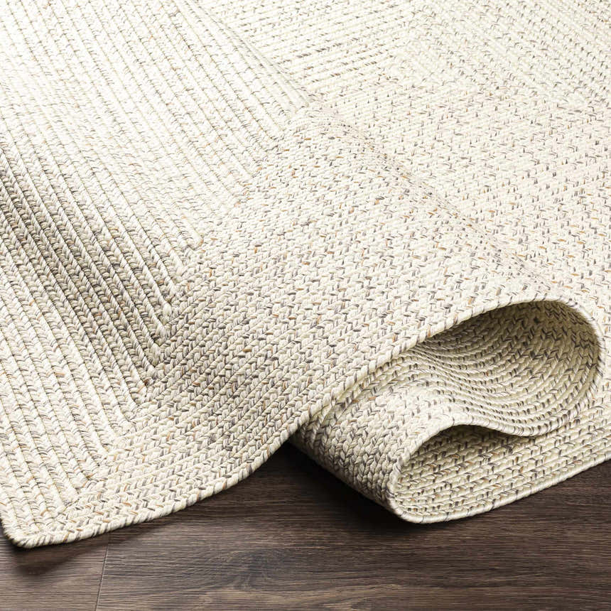 Close-up of Beige Braided Faux Jute Rug showing the texture and pattern on dark wood floor. Cream, brown, and charcoal colors. Fold