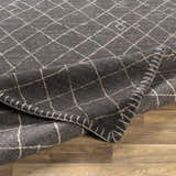 Close up of the Brimbank Premium Rug. Black wool rug with ivory geometric diamond pattern and hand-stitched edge. Fold