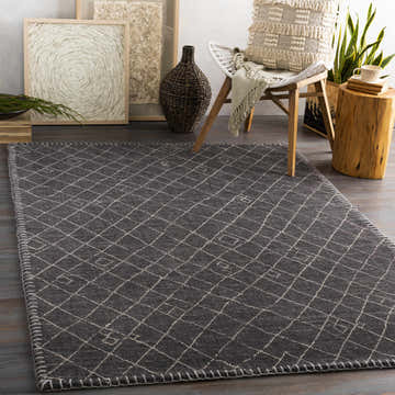 Living room scene with Brimbank Premium Rug. Black and ivory rug with diamond pattern, styled with chair, wood stool, and artwork. Roomscene-Rectangle