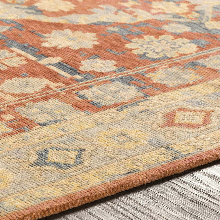 Close-up of the hand-knotted Brookeland Area Rug. Beige, brick red, and denim floral pattern on a 100% wool rug. Texture