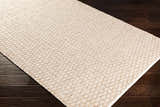 Close-up of the Brillion Area Carpet. Hand-woven polyester rug with a textured, natural fiber look on dark wood floors. Corner