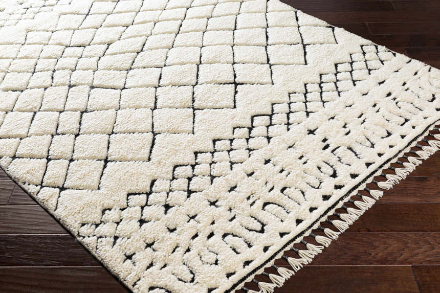 Close-up of the Brundall Clearance Rug. Cream wool rug with a black geometric Moroccan-inspired pattern and tassels. Corner