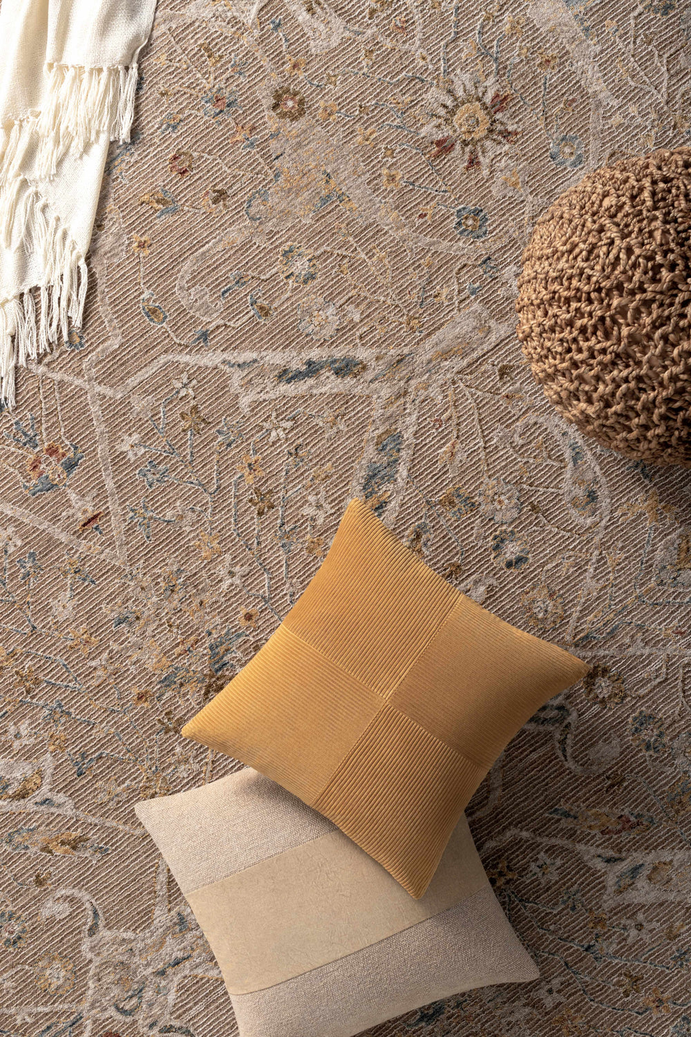Close-up of the Barneyside Luxe Area Rug in light brown with floral accents, styled with pillows and a pouf. Styleshot