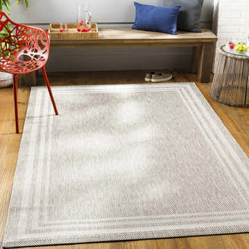 Entryway scene with a beige Burradoo Bordered Area Rug, wood bench with pillows, red chair, and woven side table. Roomscene-Rectangle