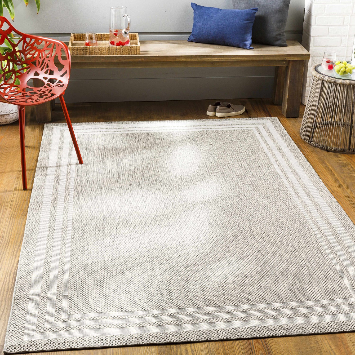 Entryway scene with a beige Burradoo Bordered Area Rug, wood bench with pillows, red chair, and woven side table. Roomscene-Rectangle