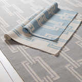 Close-up of Brundidge Area Carpet. Hand-woven wool rug in gray and ivory with contemporary geometric pattern. Runner rug partially rolled. Styleshot