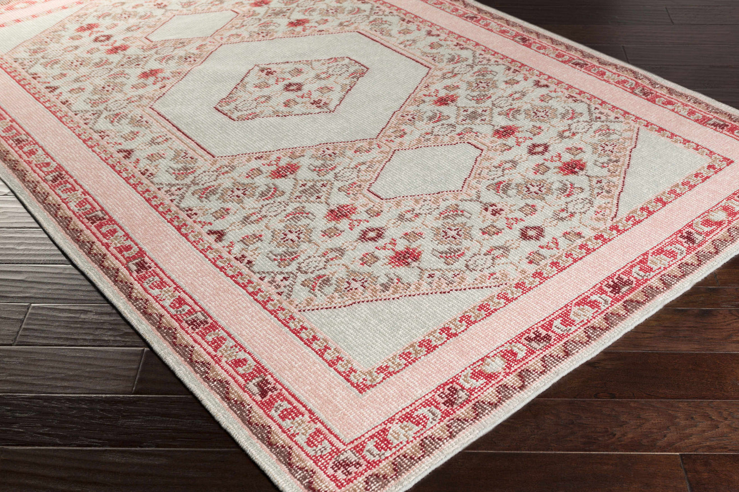 Angled view of the Bethesda Area Rug in burgundy, dusty pink, and gray on a dark wood floor. Hand-knotted wool rug. Corner