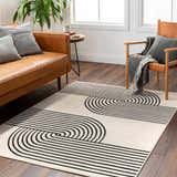 Living room scene with a Buana Area Rug, beige walls, leather sofa, and wood chair. The rug has a black geometric pattern. Roomscene-Rectangle