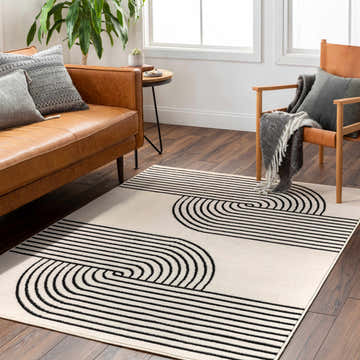 Living room scene with a Buana Area Rug, beige walls, leather sofa, and wood chair. The rug has a black geometric pattern. Roomscene-Rectangle