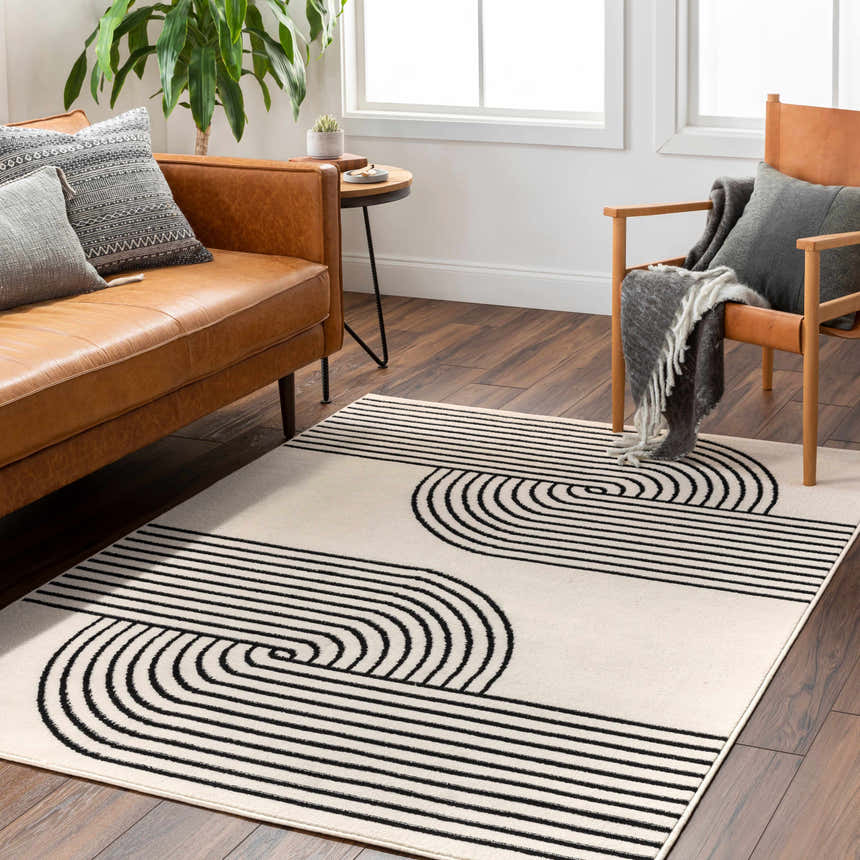 Living room scene with a Buana Area Rug, beige walls, leather sofa, and wood chair. The rug has a black geometric pattern. Roomscene-Rectangle