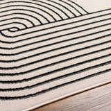 Close-up of the Buana Area Rug. Beige rug with a black geometric pattern of lines and curves. Texture