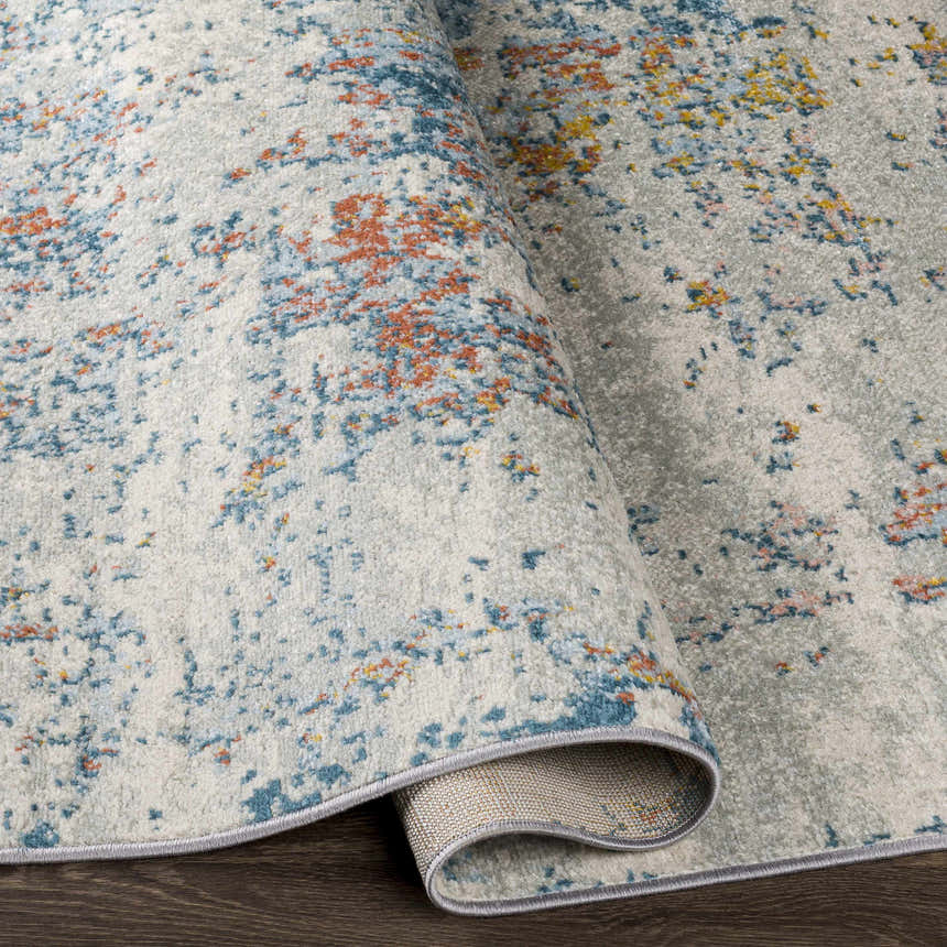 Close-up of the Buliok Area Rug, a contemporary rug with brick red, cream, blue, and yellow accents on a light gray background. Fold