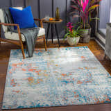 Living room scene with a Buliok Area Rug in brick red, cream, and blue, styled with a modern chair, side table, and plants. Roomscene-Rectangle