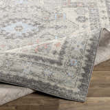Close-up of the Burham Area Rug showing its charcoal, gray, dusty pink, and pale blue traditional pattern and texture. Fold