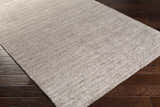 Close-up of the gray Buskirk Area Rug showing its hand-loomed texture and subtle contemporary design on dark wood flooring. Corner