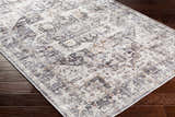 Close-up of the Bevin Washable Area Rug. Farmhouse style rug in dark brown, gray, and taupe on dark wood flooring. Corner