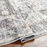 Close-up of the Bevin Washable Area Rug. Traditional style rug in dark brown, gray, and taupe tones with a detailed pattern. Fold