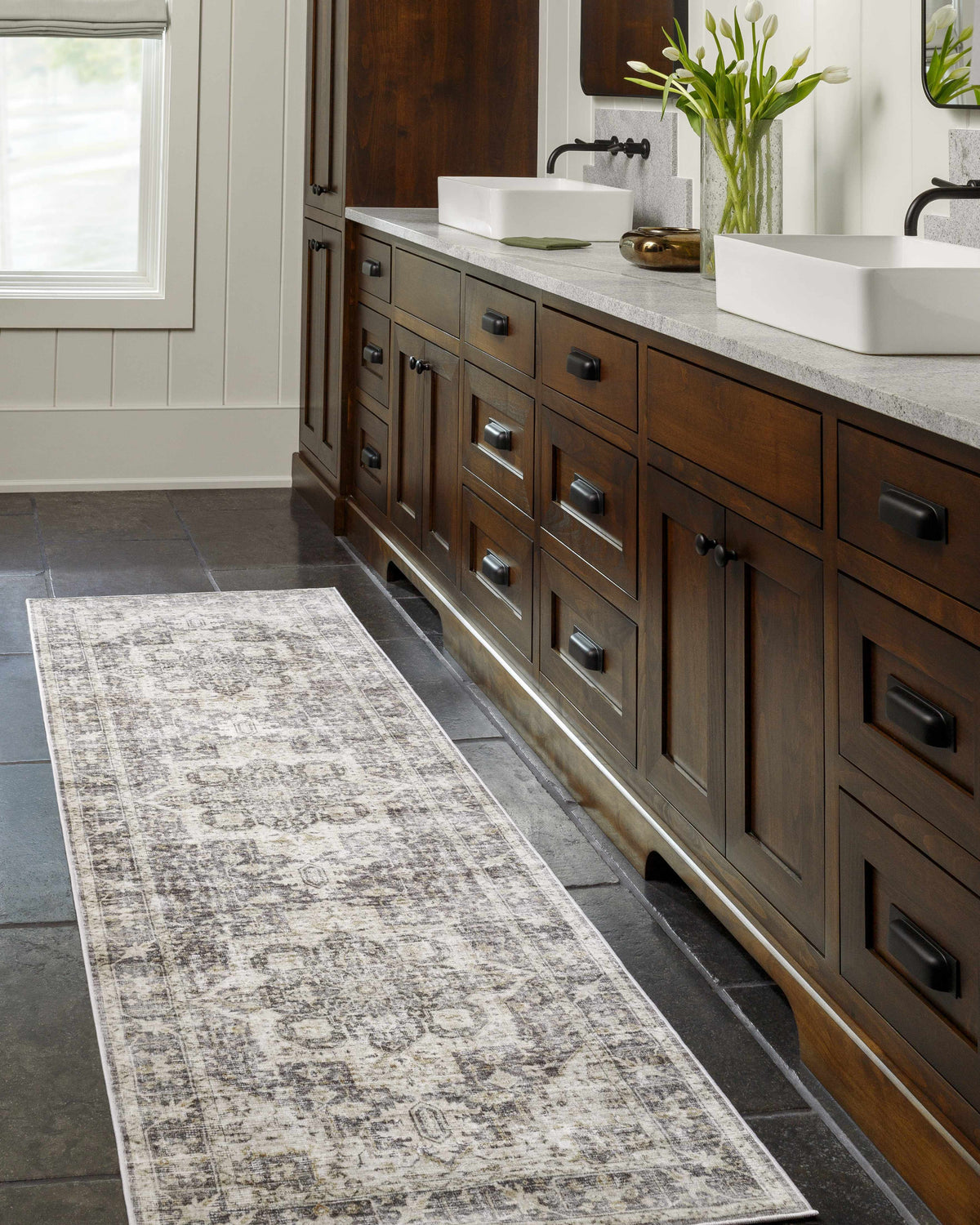 Bathroom scene with a gray and taupe Bevin Washable Area Rug runner in front of a dark wood vanity with white sinks. Roomscene-Runner