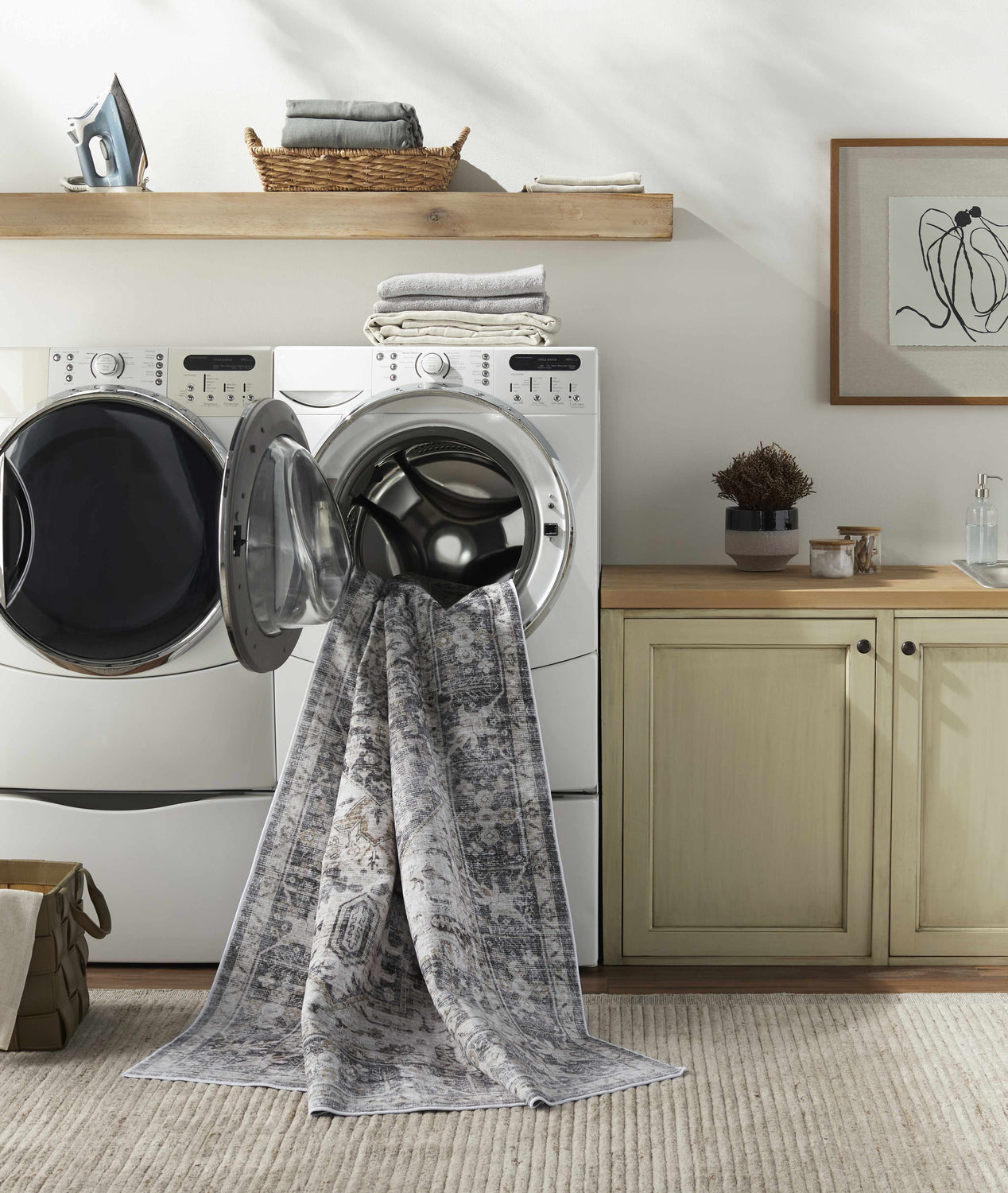 Laundry room scene with Bevin Washable Area Rug emerging from a front load washer. Farmhouse style with gray and brown tones. Washing-Machine