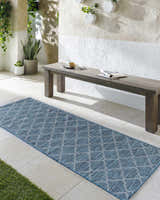 Outdoor patio scene with a teal Unique Outdoor Trellis Area Rug, wood bench, and plants. Roomscene-Runner